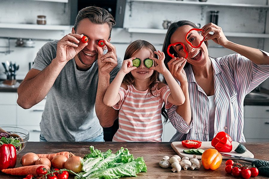 Personal Insurance - Mother Father and Small Daughter are Making Funny Faces With Vegetables While Preparing Ingredients to Cook